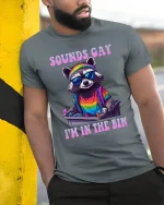 Sounds Gay I’m In The Bin Raccoon Pride T-Shirt - model leaning on yellow-black pole, wearing Gray T-shirt, hand in pocket