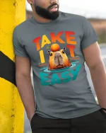 Take It Easy Capybara Relaxed Funny Graphic T Shirt Design - model wearing grey tee, leaning on column