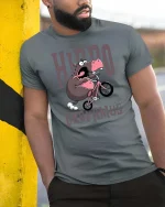 Hippo Dropamus Funny Hippo Riding Bike Cartoon T-Shirt - model wearing grey tee, leaning on column