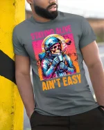 Staying Alive Ain’t Easy Funny Astronaut Skull T-Shirt - model wearing grey tee, leaning on column