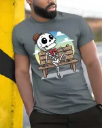 Funny Skeleton Bench T-Shirt Cute Cartoon Skull Graphic - model wearing grey tee, leaning on column