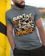 Burnt Out But Optimistic Raccoon T-Shirt Funny Graphic - model wearing grey tee, leaning on column