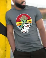 Alien Cowboy Riding Cow Funny Retro Sunset Graphic T-Shirt - model wearing grey tee, leaning on column